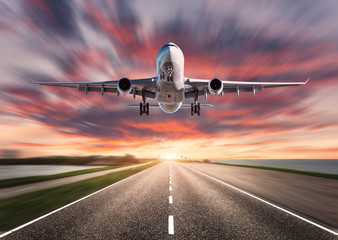 Airplane and road with motion blur effect at sunset. Landscape with passenger airplane is flying...