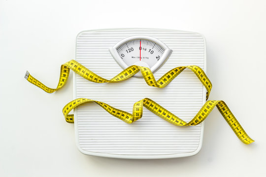 Diet concept with scale and measuring tape for weight loss on white background top view