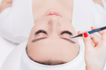 Eyelash Extension Procedure. Close up view of female eyes with long eyelashes. Stylist holding tweezers, tongs and making lengthening lashes. Macro, selective focus.