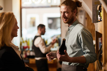 Waist up portrait of smiling young man consulting customer in liquor store, copy space