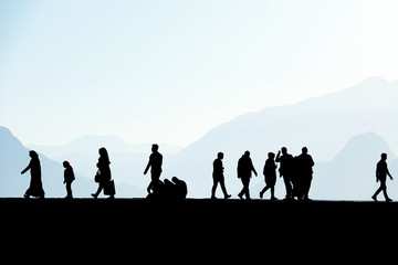 Silhouetted people walking and relaxing on street over sunny morning sky with high mountains in Antalya, Turkey