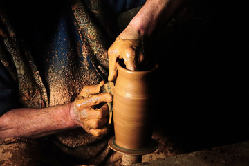 Close up mud covered hands of adult man making clay pot on potter's wheel