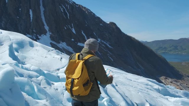 Bearded man with a yellow backpack and a tourist map in his hands, against the backdrop of the winter landscape