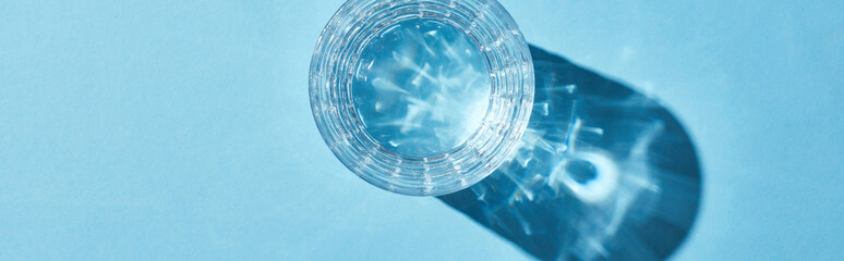 top view of glass with clear water on blue background with shadow, panoramic shot