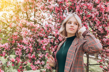 Close up portrait of young pretty caucasian curly blondie model posing outdoors in pink blossom garden. Beauty, nature concept