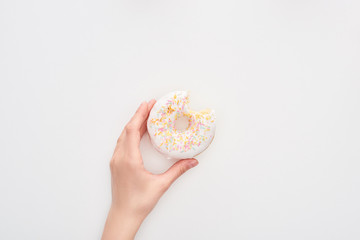 Fototapeta na wymiar partial view of woman holding glazed bitten white doughnut with sprinkles on white background