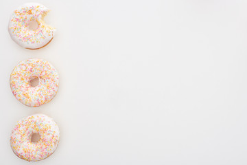 top view of tasty whole doughnuts with sprinkles near bitten one on white background