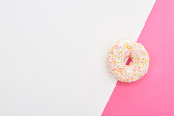 top view of glazed white doughnut with sprinkles on white and pink background with copy space