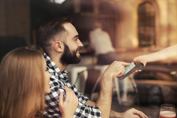 Man with credit card using payment terminal at restaurant, view through window