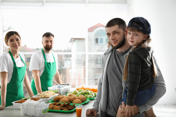 Poor father and daughter receiving food from volunteers indoors