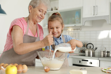 Cute girl and her grandmother cooking in kitchen