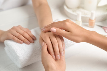 Fototapeta na wymiar Cosmetologist massaging client's hand at table in spa salon, closeup