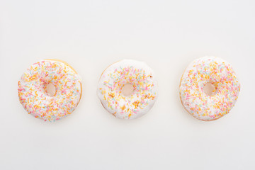 top view of glazed white doughnuts with sprinkles on white background