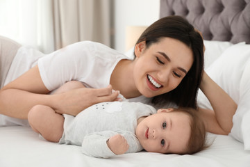 Portrait of mother with her cute baby lying on bed indoors