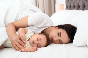 Mother and her cute baby sleeping on bed indoors