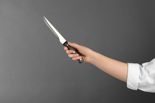 Woman holding carving knife on grey background, closeup. Space for text