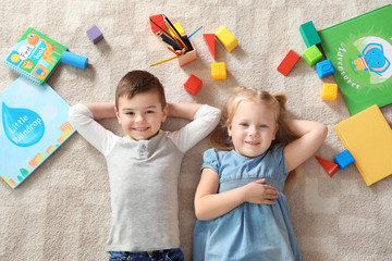 Little children with toys and books lying on carpet indoors, top view. Playtime