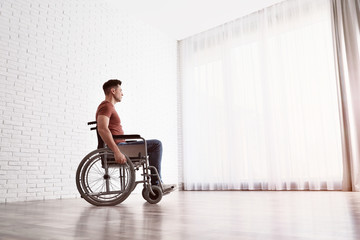 Thoughtful man sitting in wheelchair near window at home