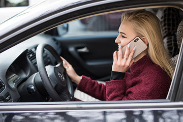 Cheerful young woman driving a car and talking on the phone