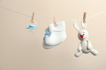 Knitted booties, pacifier and toy bunny hanging on washing line against color background. Baby...