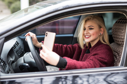 Smiling young woman taking selfie picture with phone camera outdoors in car