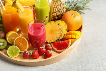 Wooden tray with glasses of different juices and fresh fruits on table