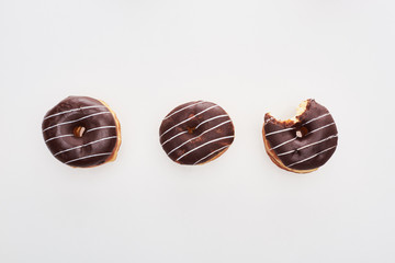 top view of chocolate tasty whole doughnuts near bitten one on white background