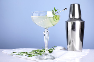 Glass of cucumber martini, shaker and rosemary on table against color background, space for text