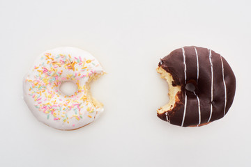 top view of bitten chocolate and white doughnuts on white background