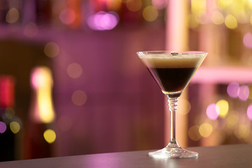 Glass of Espresso Martini on counter in bar, space for text. Alcohol cocktail