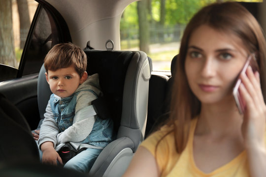 Mother Talking By Phone While Driving Car With Her Son On Backseat. Child In Danger