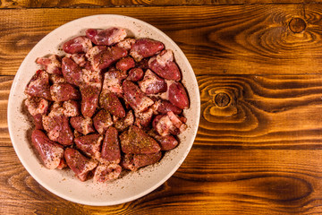 Ceramic plate with raw chicken hearts on wooden table. Top view