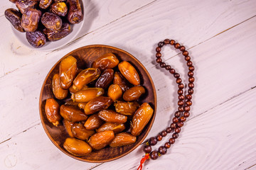 Date fruits and rosary on wooden table. Top view