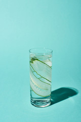 transparent glass with pure water and cucumber slices on turquoise background