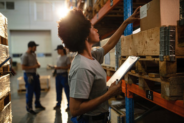 African American female worker checking packages in distribution warehouse.