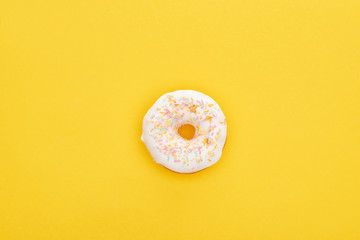 top view of tasty white glazed doughnut with sprinkles on bright yellow background