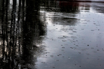 the pouring rain, with a thunderstorm and a thunder, water flows on asphalt forming pools, drops of a rain get to pools and splashes fly rereflecting light from the sun