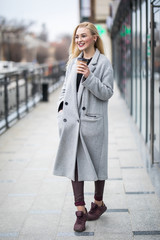 Young woman wearing a coat holds a cup hot beverage on a cold day