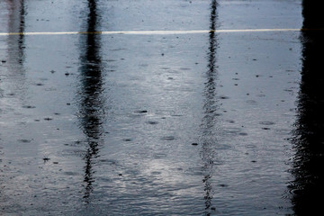 the pouring rain, with a thunderstorm and a thunder, water flows on asphalt forming pools, drops of a rain get to pools and splashes fly rereflecting light from the sun