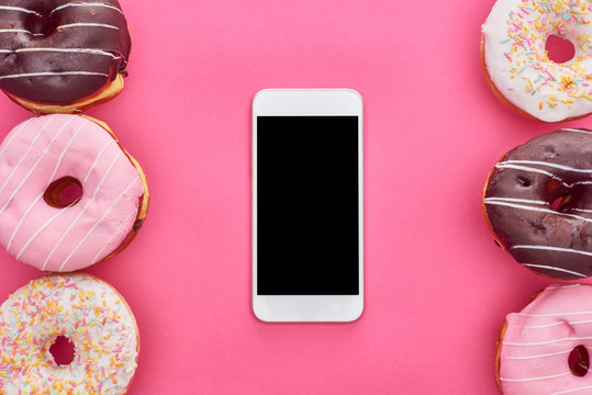 top view of tasty glazed doughnuts and smartphone with blank screen on bright pink background