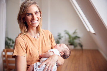 Portrait Of Loving Mother Holding Newborn Baby At Home In Loft Apartment