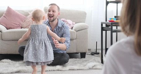 Happy parents with baby daughter learning to walk at home