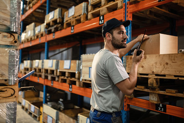 Male dispatcher communicating over walkie-talkie while working in a warehouse. - obrazy, fototapety, plakaty