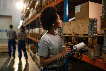 Female warehouse employee checking stock of packages on shelfs.