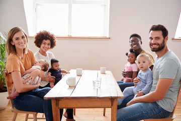 Portrait Of Two Families With Babies Meeting Around Table On Play Date At Home