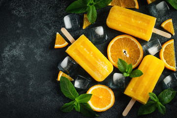 Bright popsicle made of oranges on a dark concrete background. Sweet summer treat. Top view with...