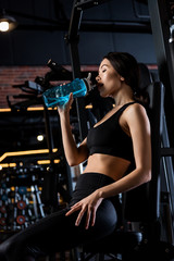 Fototapeta na wymiar low angle view of attractive woman in sportswear drinking water from sport bottle