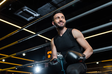 Fototapeta na wymiar low angle view of handsome man in boxing gloves smiling in gym
