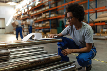 Black female worker checking list of products in a warehouse.