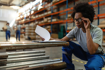 African American woman going through paperwork while working in a warehouse.